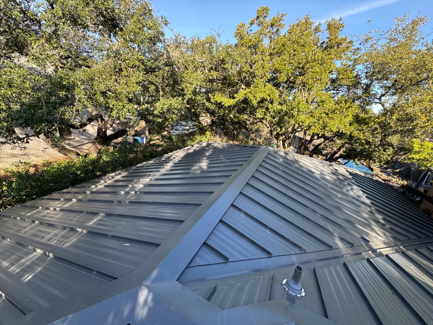 Charcoal standing seam metal roof aerial at golden hour under live oaks on a recent Austin Area Roofers job