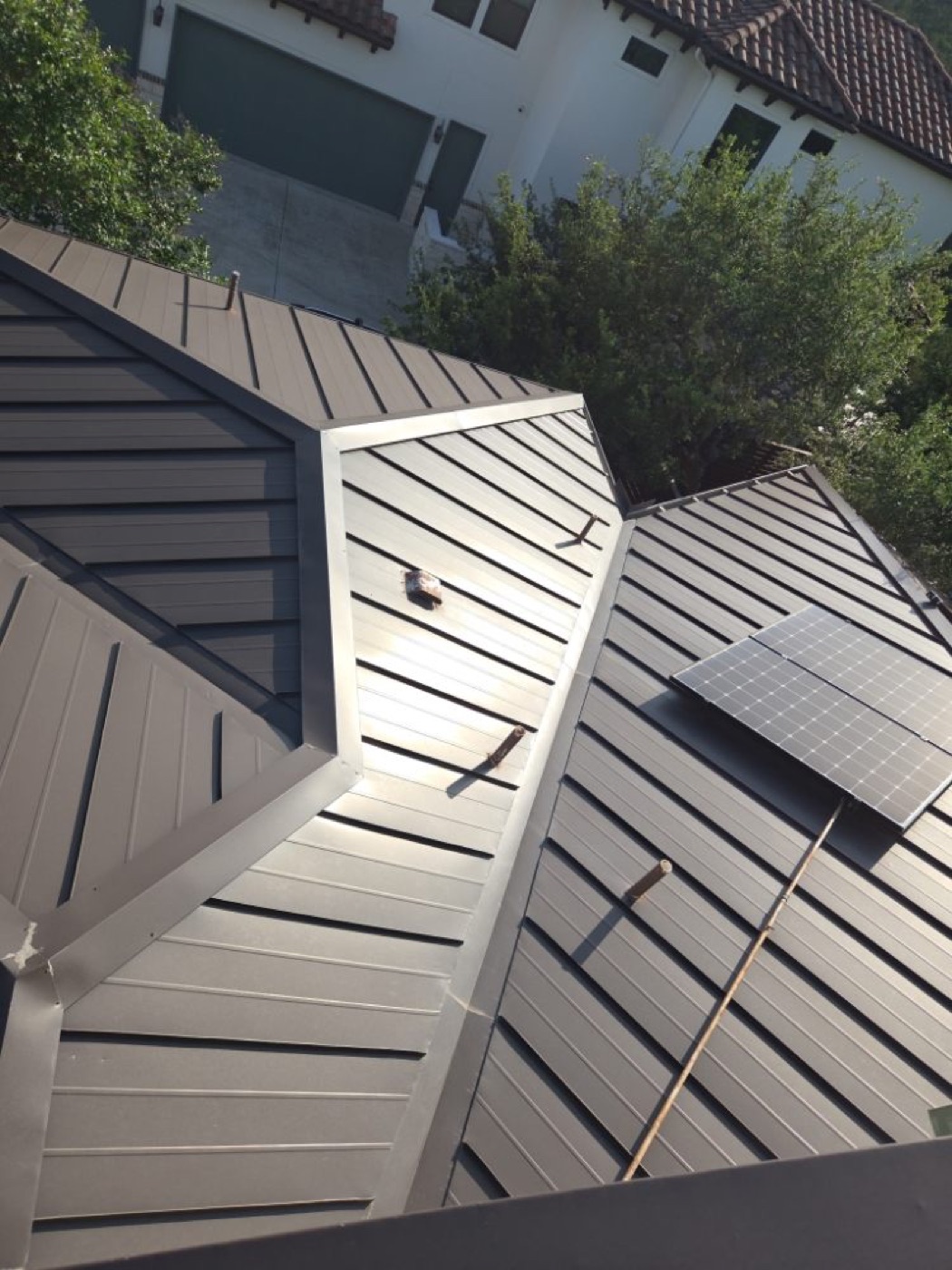 Aerial of a dark-bronze standing seam metal roof in Dripping Springs with multi-plane geometry and a solar panel array