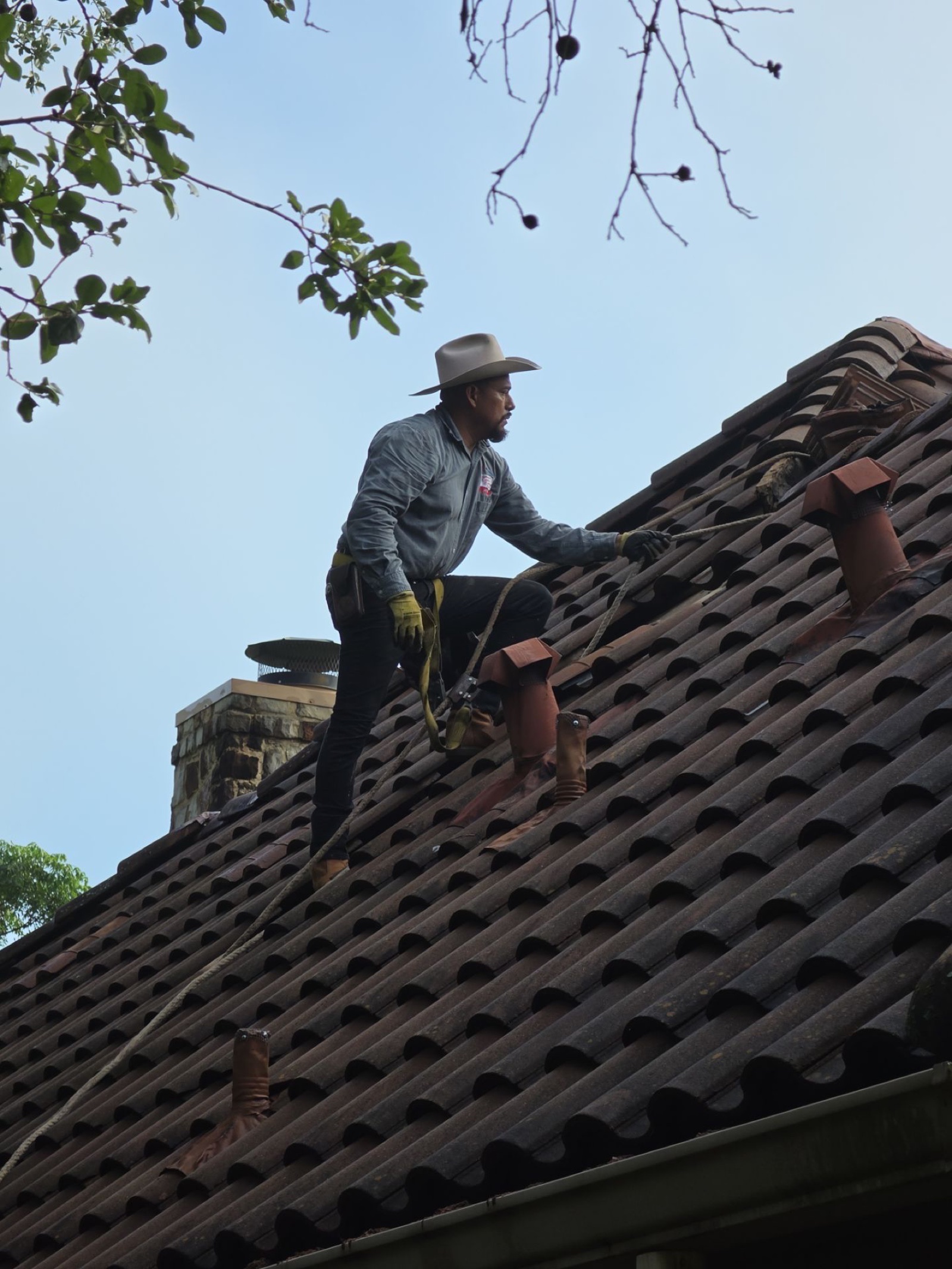 Founder Benny in the hat, roped to a West Austin tile ridge with harness and tool belt · he walks every job himself