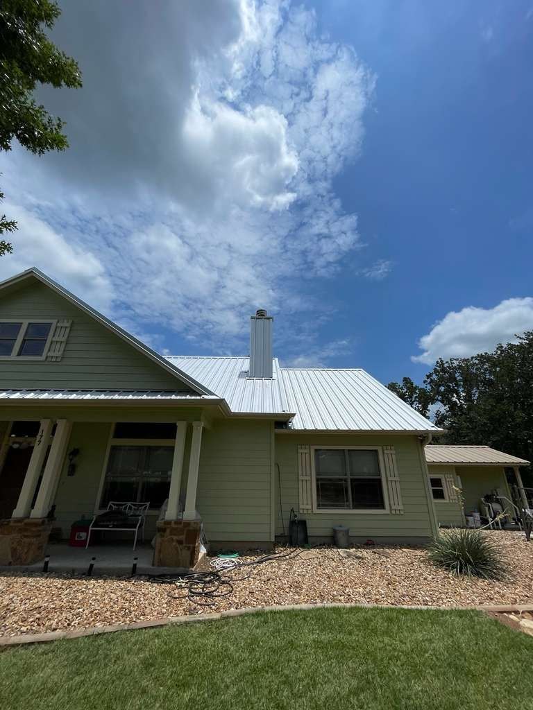 Finished light-grey standing seam metal roof on a sage-green Central Texas home with hand-wrapped chimney