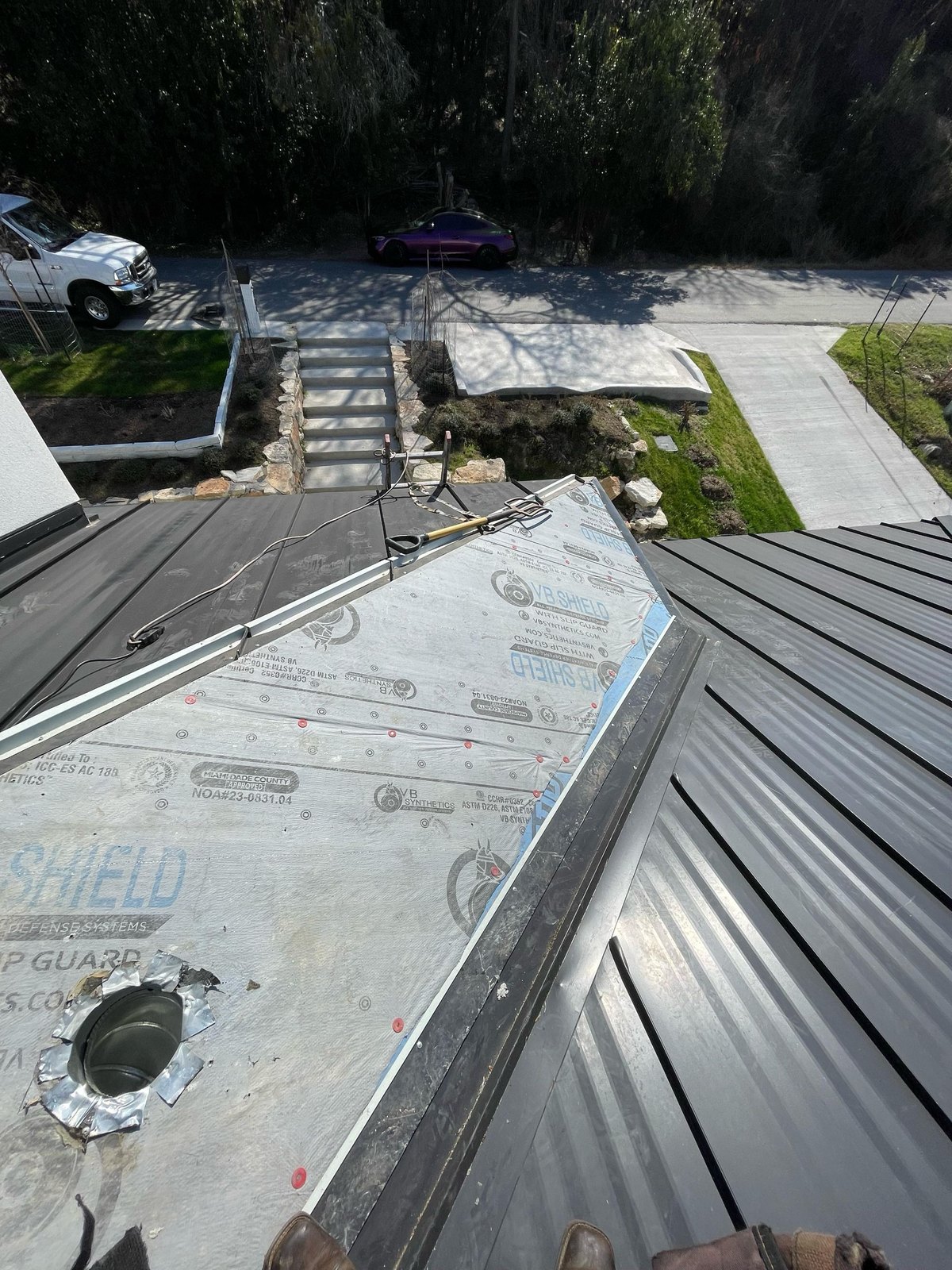 Mid-install multi-plane metal roof showing VB Shield underlayment beneath the new dark panels