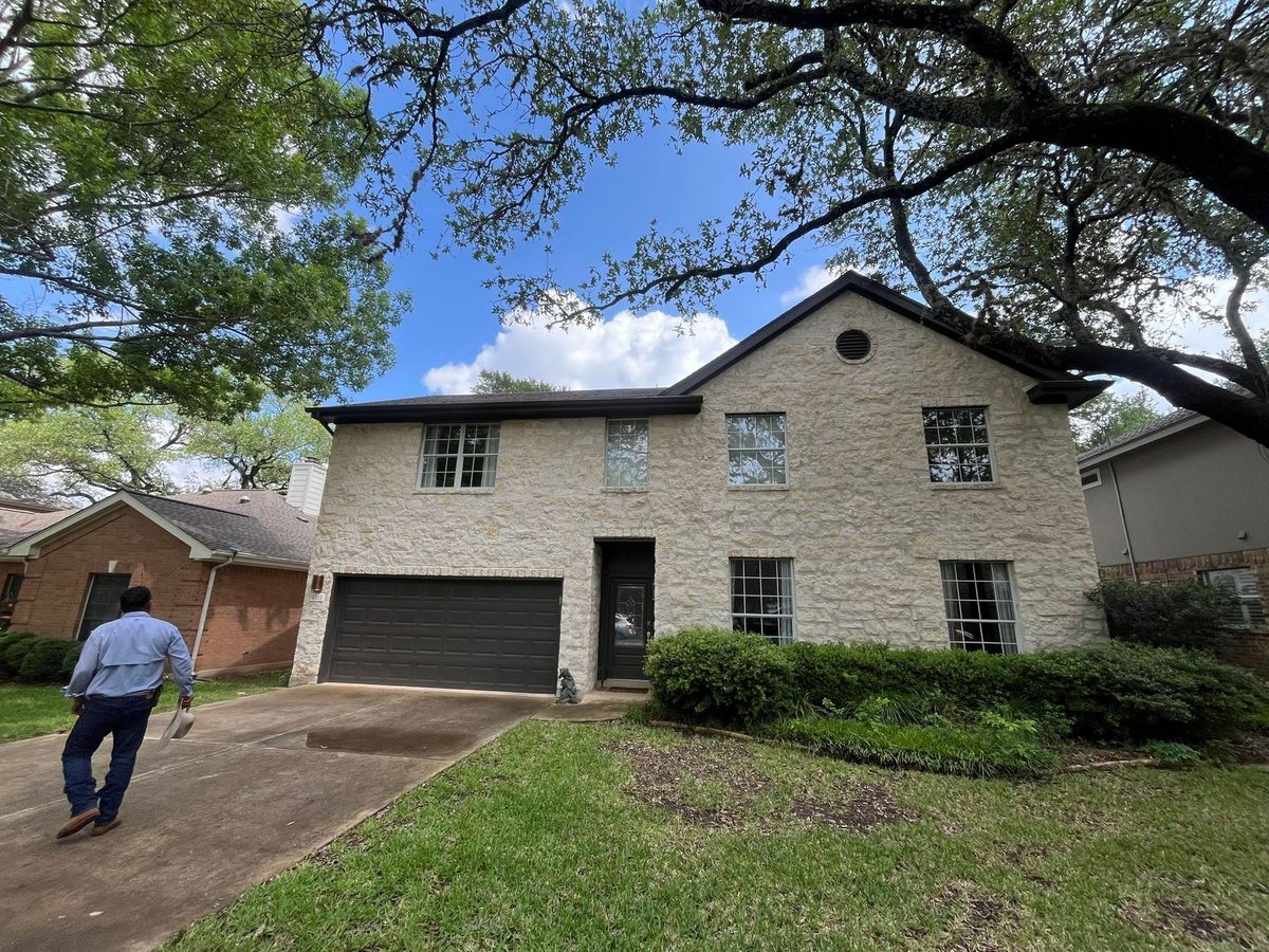 Austin Area Roofers founder Benny walking up to a two-story stone home in Tarrytown, Austin for a free roof inspection