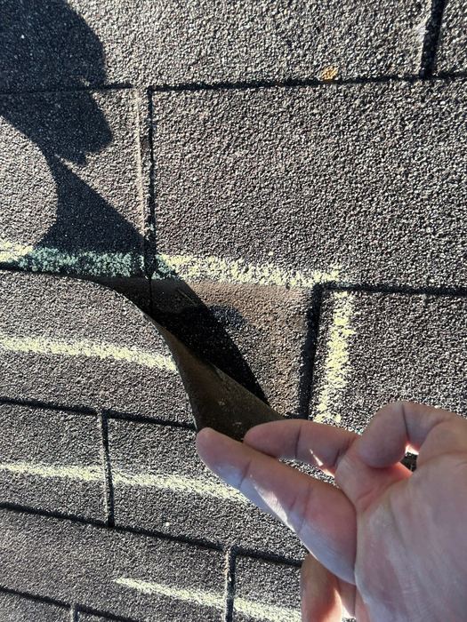 Hand peeling back a hail-damaged architectural shingle to show seal failure on a Pflugerville roof inspection