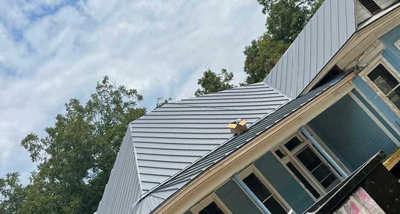 Light-grey standing seam metal roof installed by Austin Area Roofers on a blue Austin home · 22-gauge G90 galvalume install, mid-project from REPS CompanyCam library