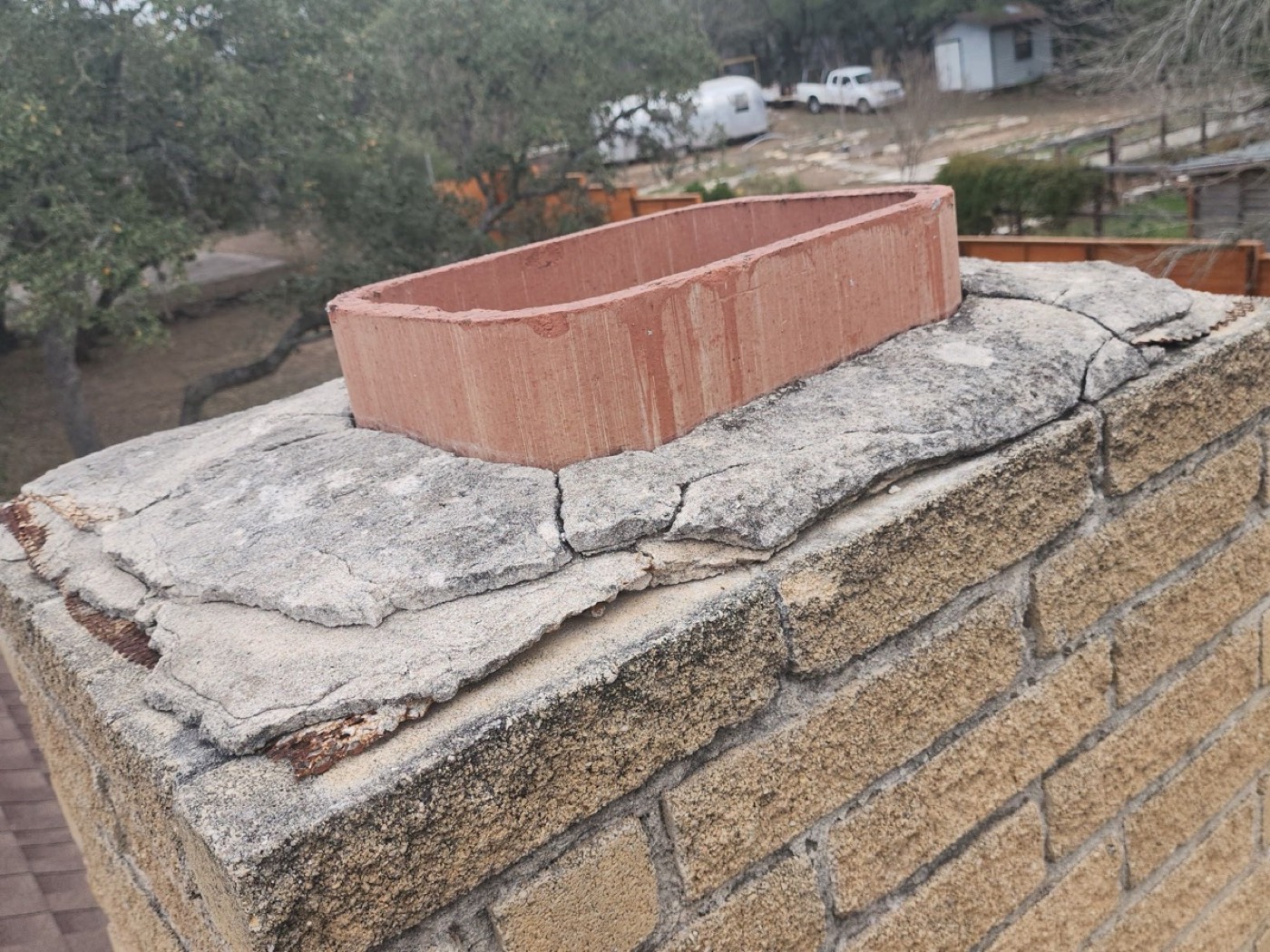 Fractured masonry chimney crown on El Rey Blvd with a structural crack across the wash, the failure mode that loses flashing integrity even with new step flashing installed.