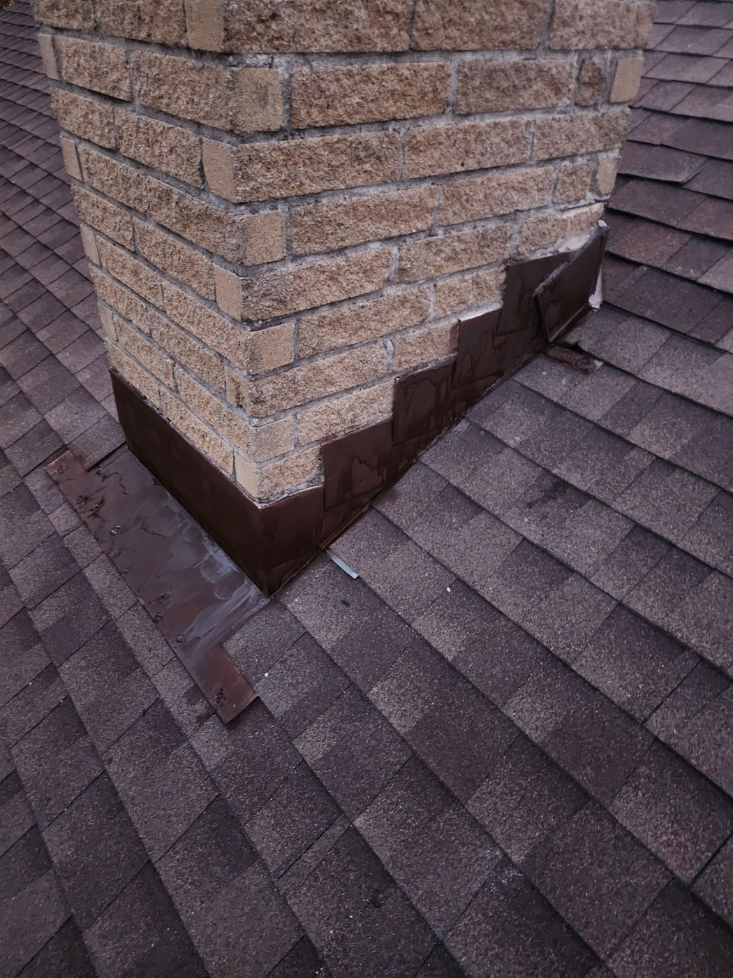New step flashing installed at the chimney-to-roof intersection on the same Lock Lynnhe project, hand-folded brown and integrated into a fresh shingle field with a clean step lap.