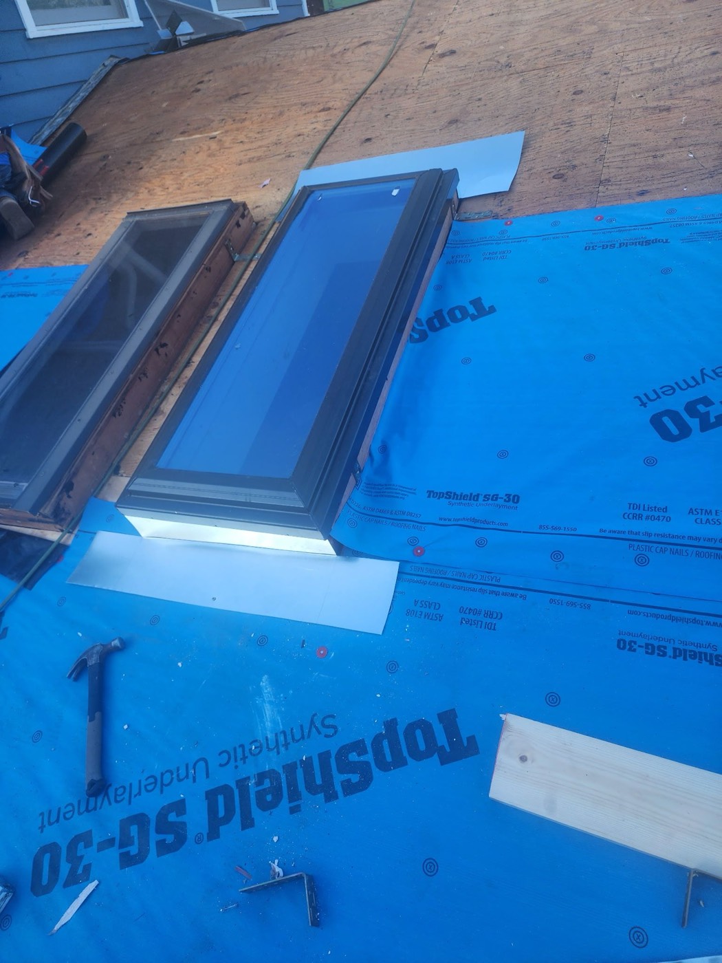 Two skylights set into the roof field with the new TopShield SG-30 synthetic underlayment laid around them, documented mid-install. Skylight replacement filed and approved as a separate supplement line.