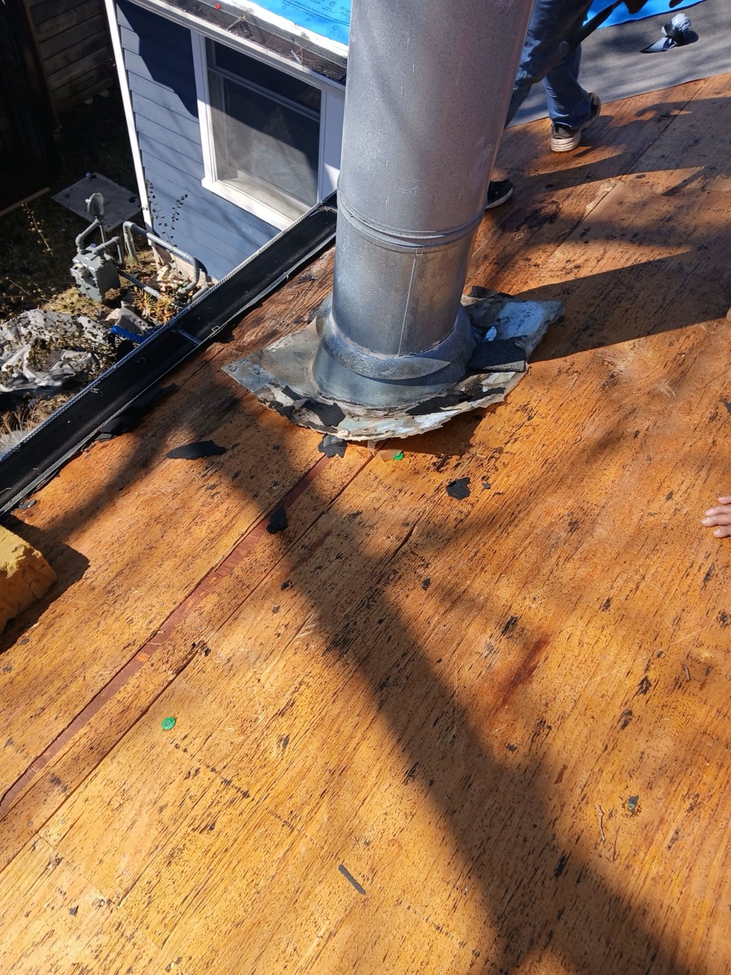 Galvanized B-vent with a rusted lead flange and visible hail dimples on the collar, documented on dark stained sheathing during tear-off. Approved as a separate line item for the supplement.